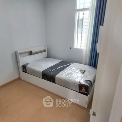Cozy bedroom with a single bed and natural light from a tall window, perfect for a restful retreat.