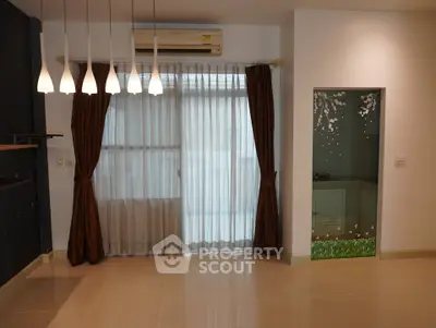 Spacious living room with elegant lighting and large window draped with curtains.