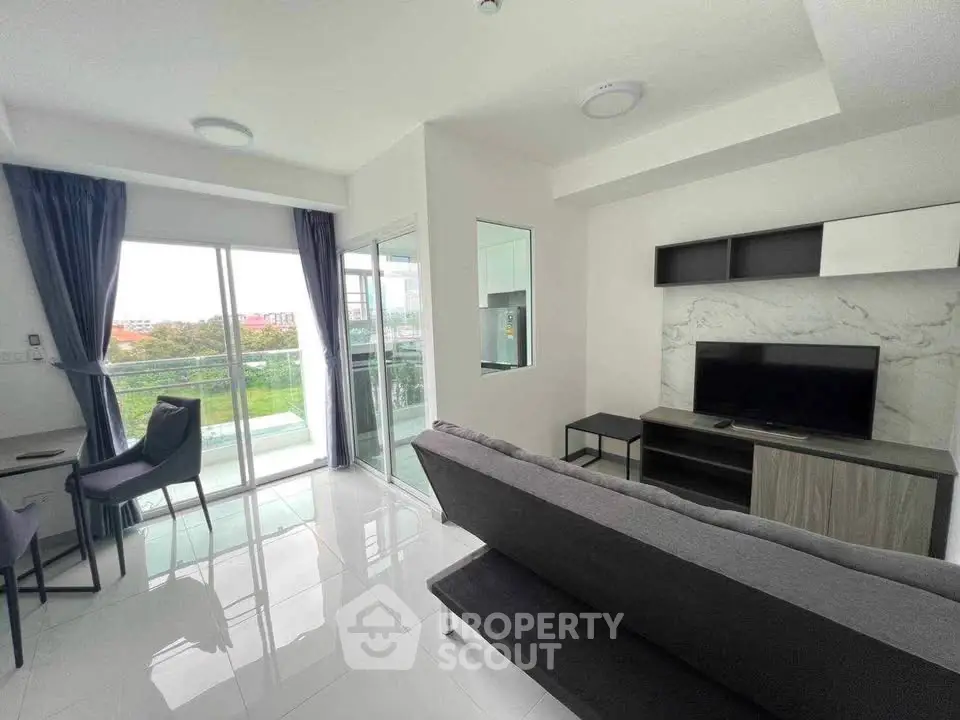 Modern living room with sleek design and balcony view, featuring a comfortable sofa and flat-screen TV.