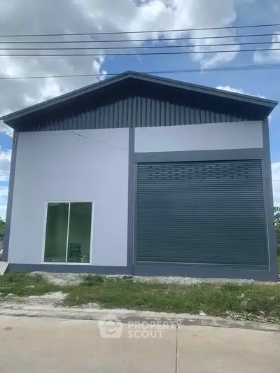 Modern industrial-style building with large roller door and glass window, ideal for commercial use.