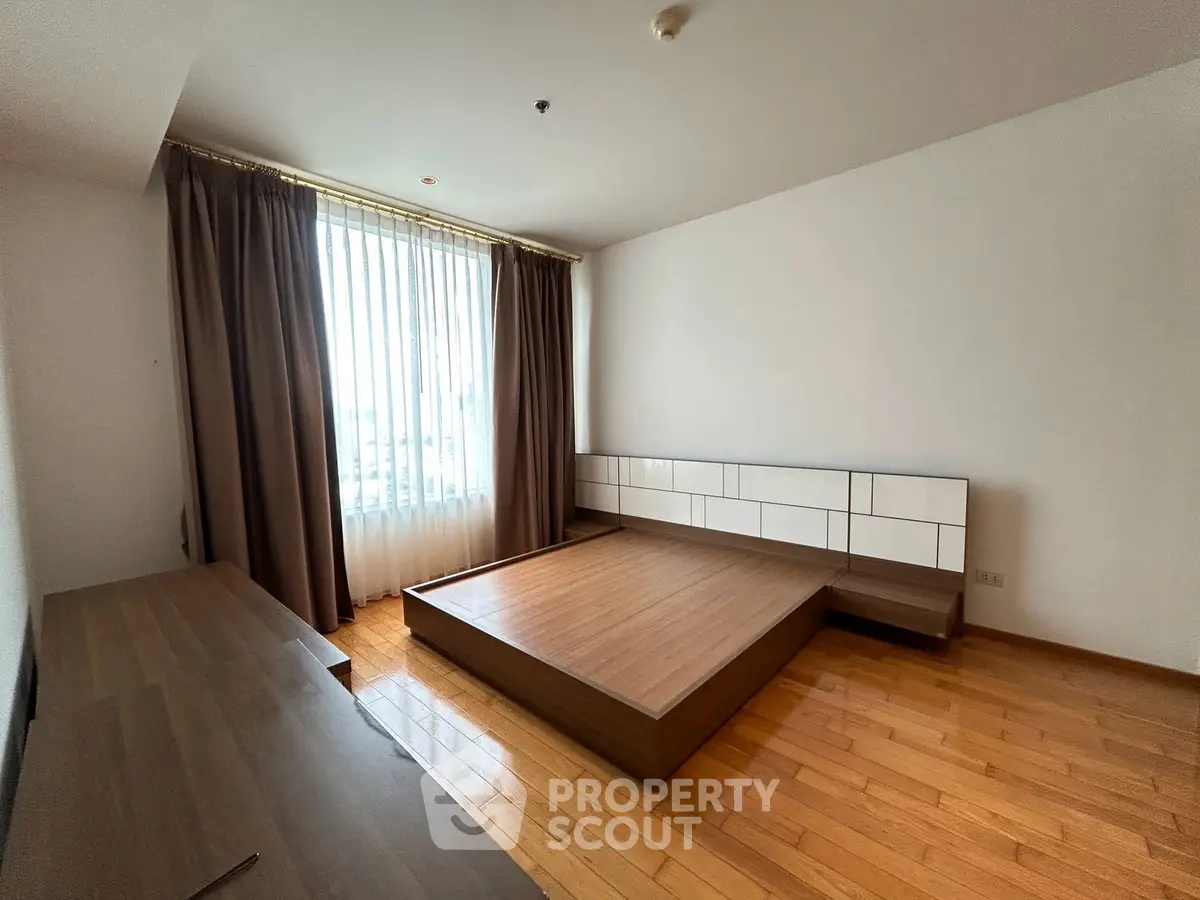 Spacious bedroom with wooden flooring and large window in modern apartment