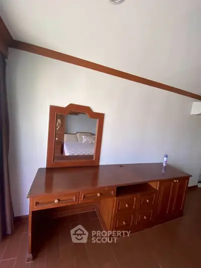 Spacious bedroom with elegant wooden furniture and mirror, perfect for a cozy and stylish living space.