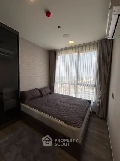 Cozy bedroom with large window offering city view, featuring modern decor and air conditioning.