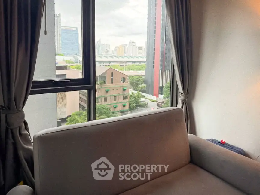 Cozy living room with city view through large window, featuring a comfortable sofa and elegant curtains.