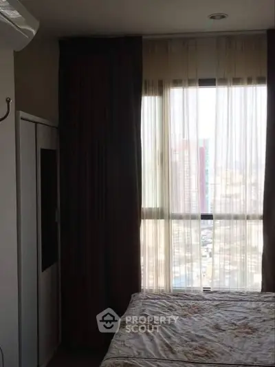 Cozy bedroom with large window offering city view and natural light.
