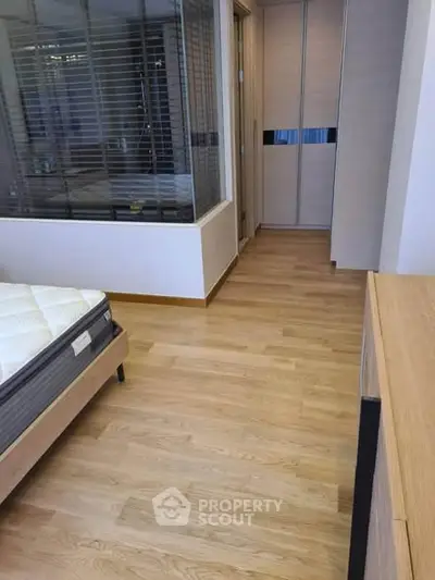 Modern bedroom with wooden flooring and glass partition, featuring a comfortable mattress and sleek wardrobe.