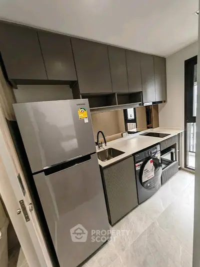 Modern kitchen with sleek cabinets, stainless steel fridge, and washing machine in a compact layout.