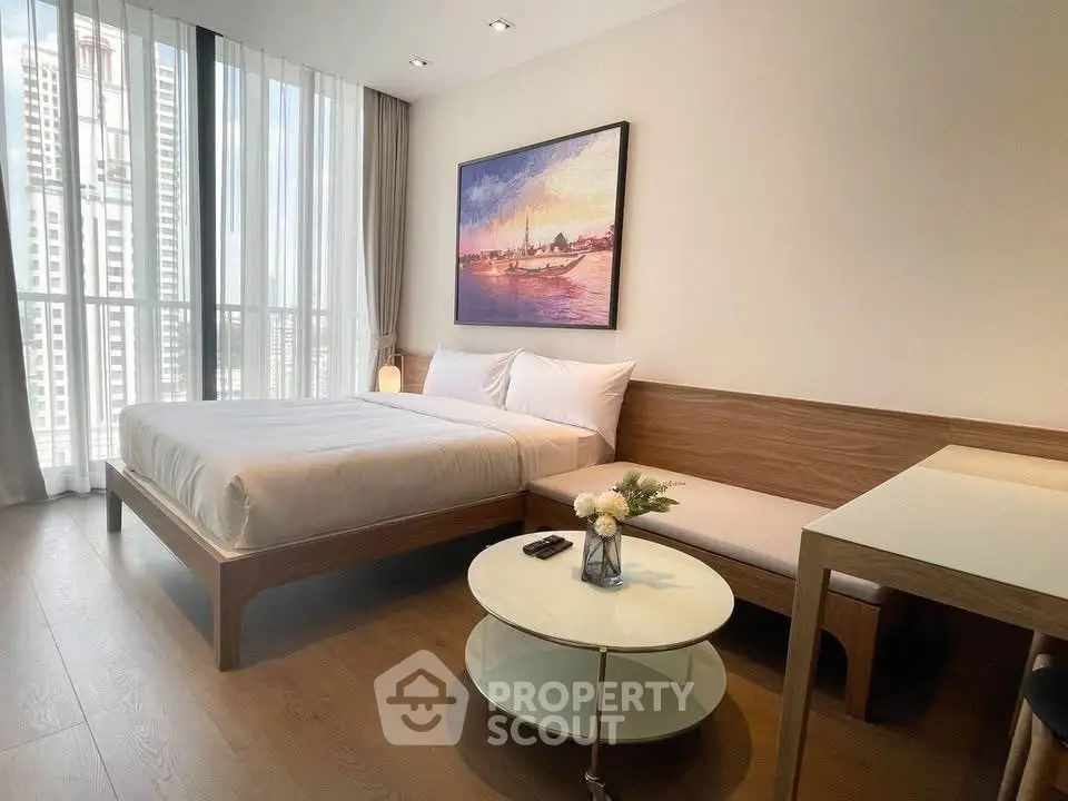 Modern bedroom with large window, stylish decor, and cozy seating area.