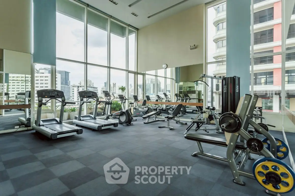 Spacious modern gym with large windows and city view, featuring state-of-the-art fitness equipment.