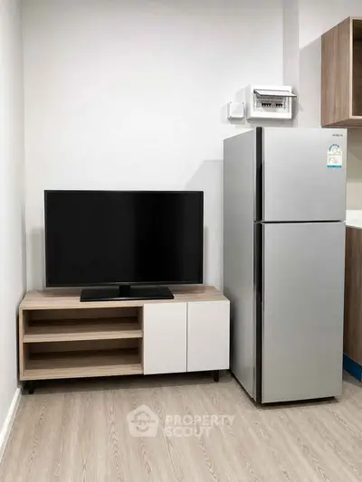 Modern apartment interior with sleek TV stand and stainless steel fridge, showcasing minimalist design.