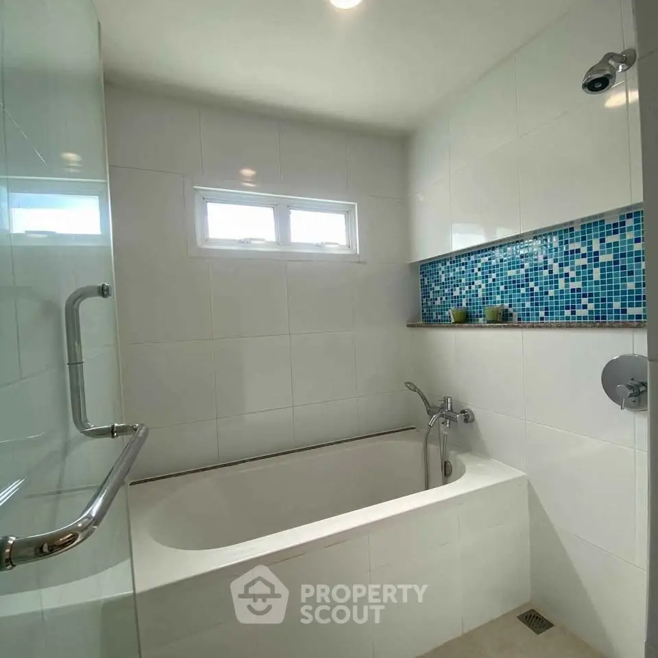 Modern bathroom with sleek bathtub and stylish blue mosaic tile accent.
