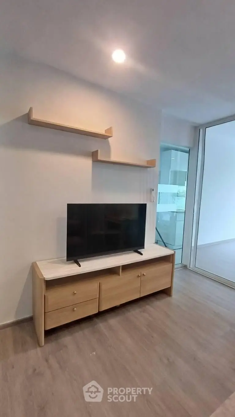 Modern living room with sleek TV stand and floating shelves, featuring glass sliding doors and wooden flooring.