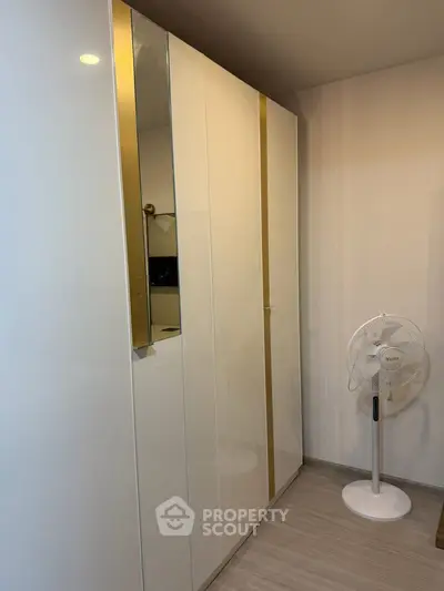 Modern bedroom with sleek white wardrobe and standing fan, perfect for minimalist living.