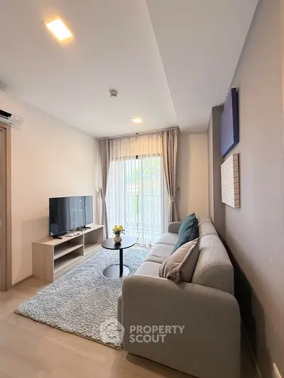 Modern living room with cozy sofa, TV, and natural light from large window.