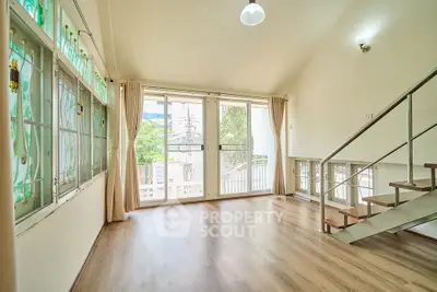 Spacious living room with large windows and modern staircase, offering abundant natural light and elegant design.