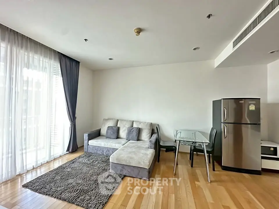 Modern living room with stylish sofa, glass dining table, and sleek refrigerator in a bright apartment.
