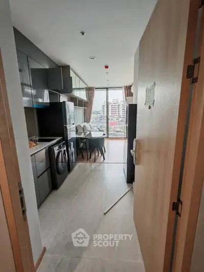 Modern apartment entrance leading to a sleek kitchen and dining area with city view.