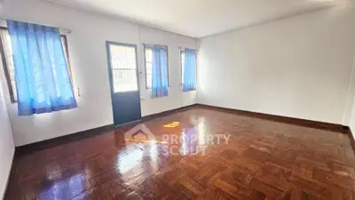Spacious empty room with wooden flooring and blue curtains, ideal for customization.