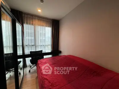 Cozy bedroom with red bedding and study desk, featuring large windows for natural light.