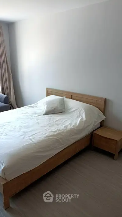 Modern bedroom with wooden bed frame and side table, featuring minimalist design and natural light.