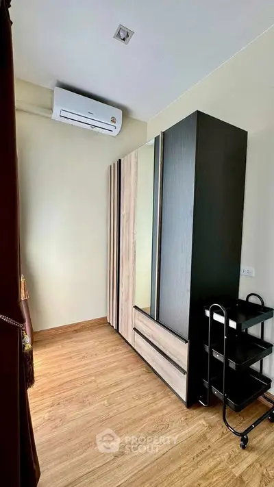 Modern bedroom with sleek wardrobe and air conditioning unit, featuring wooden flooring and neutral tones.