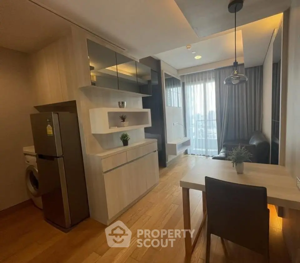 Modern living room with open kitchen, featuring sleek furniture and natural light from large windows.