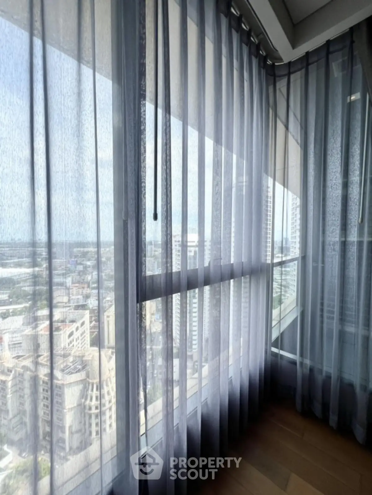 Stunning high-rise view through sheer curtains in modern apartment corner unit.