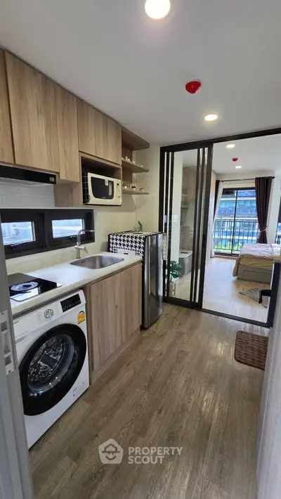 Modern compact kitchen with washing machine and open layout leading to cozy bedroom with balcony view.