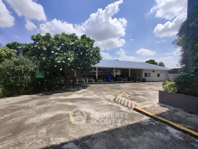 Spacious outdoor area with lush greenery and ample parking space under a clear blue sky.