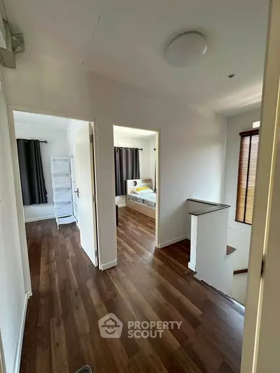 Spacious hallway with wooden flooring leading to a cozy bedroom with natural light.