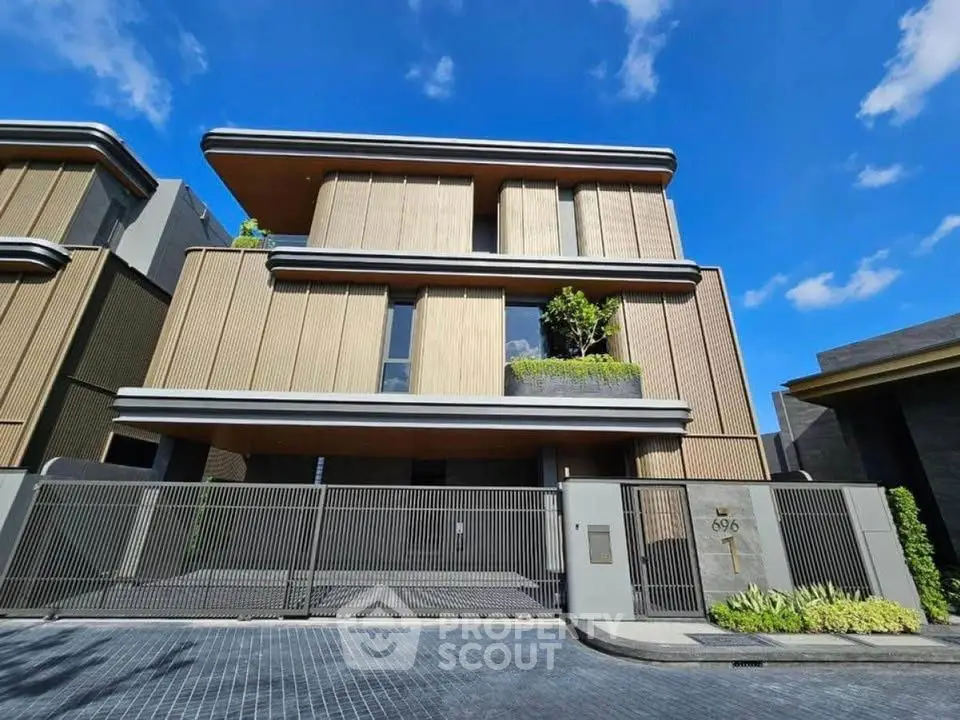 Luxurious modern three-story house with sleek design and gated entrance under a clear blue sky.