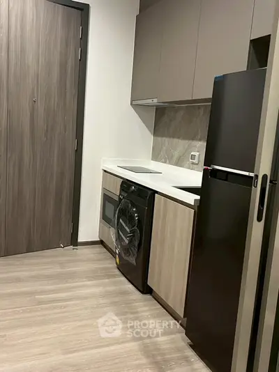 Modern kitchen with sleek appliances and wood cabinetry, featuring a washing machine and fridge.
