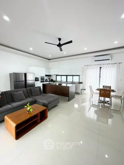 Spacious modern living room with open kitchen and dining area, featuring sleek furniture and bright lighting.
