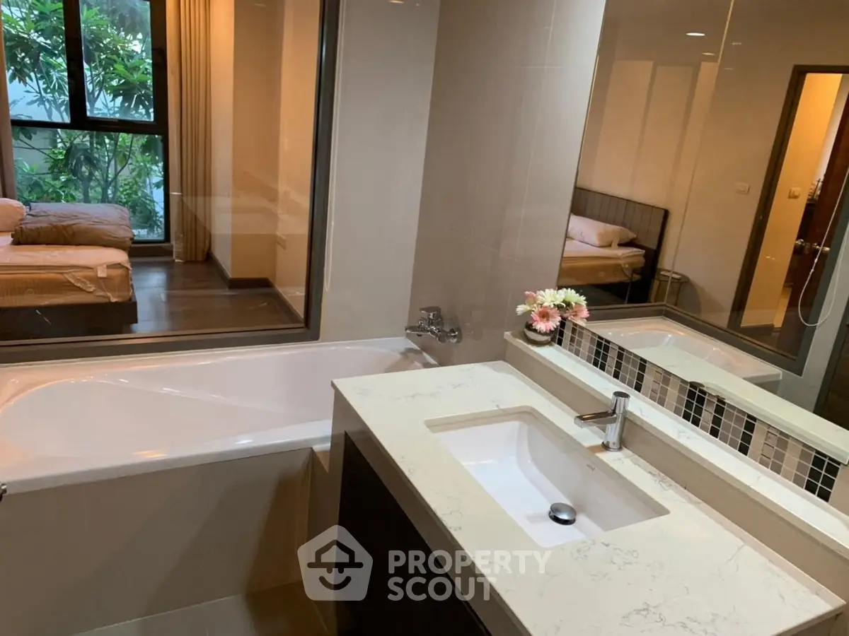 Modern bathroom with bathtub and view into cozy bedroom