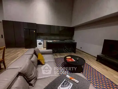 Modern living room with sleek kitchen and stylish furniture, featuring a washing machine and elegant decor.