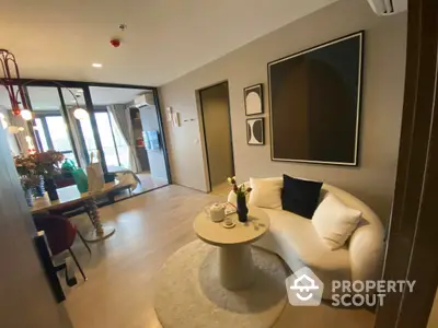 Chic modern living room with plush white sofa, elegant round coffee table, and tasteful wall art, leading to a sunlit balcony with city views.