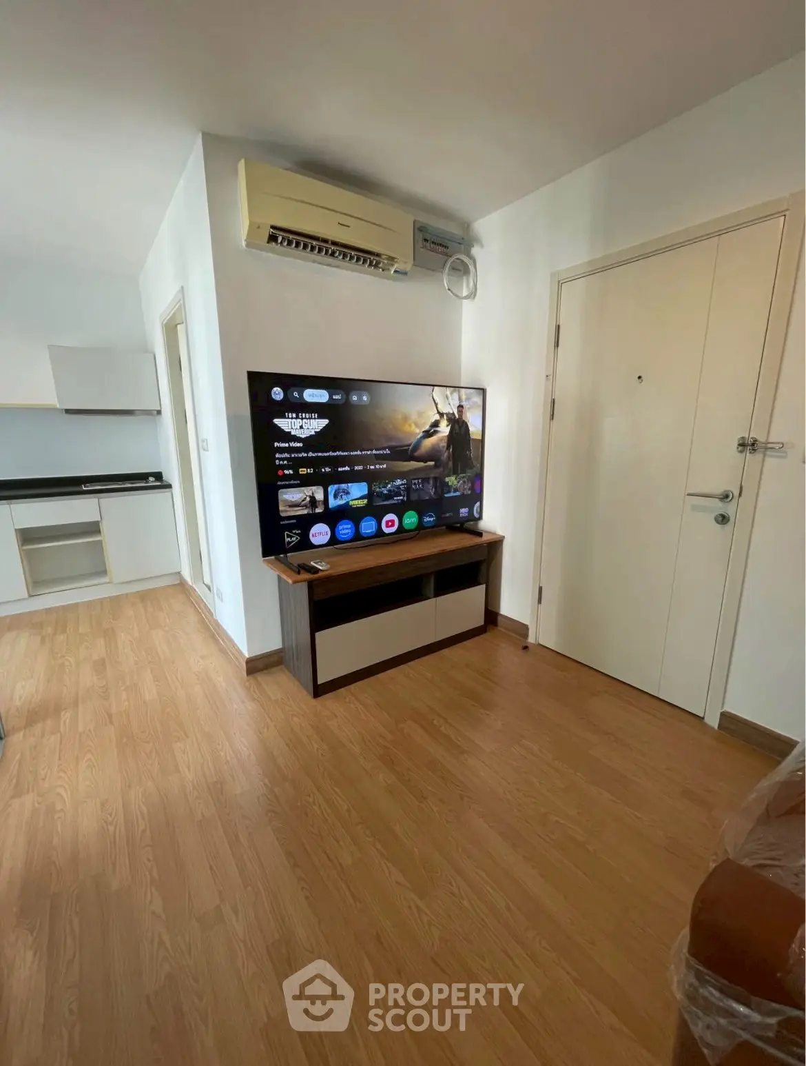 Modern living room with wooden flooring, wall-mounted TV, and air conditioning unit.