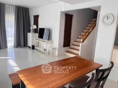Modern living room with wooden dining table and staircase, featuring sleek design and natural light.