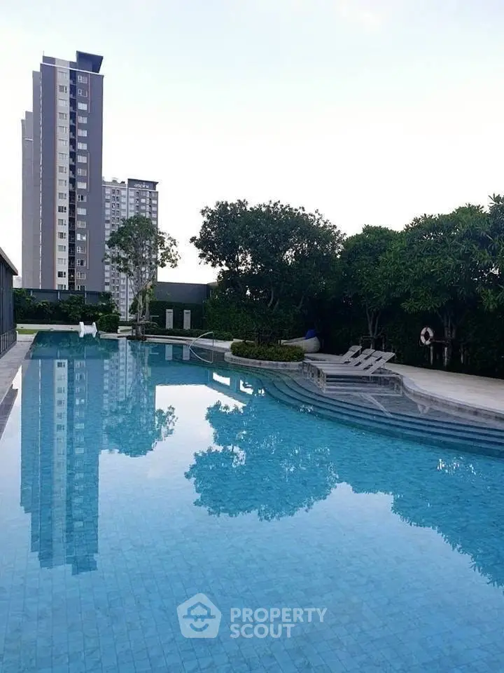 Luxurious residential pool with modern high-rise building view, surrounded by lush greenery.