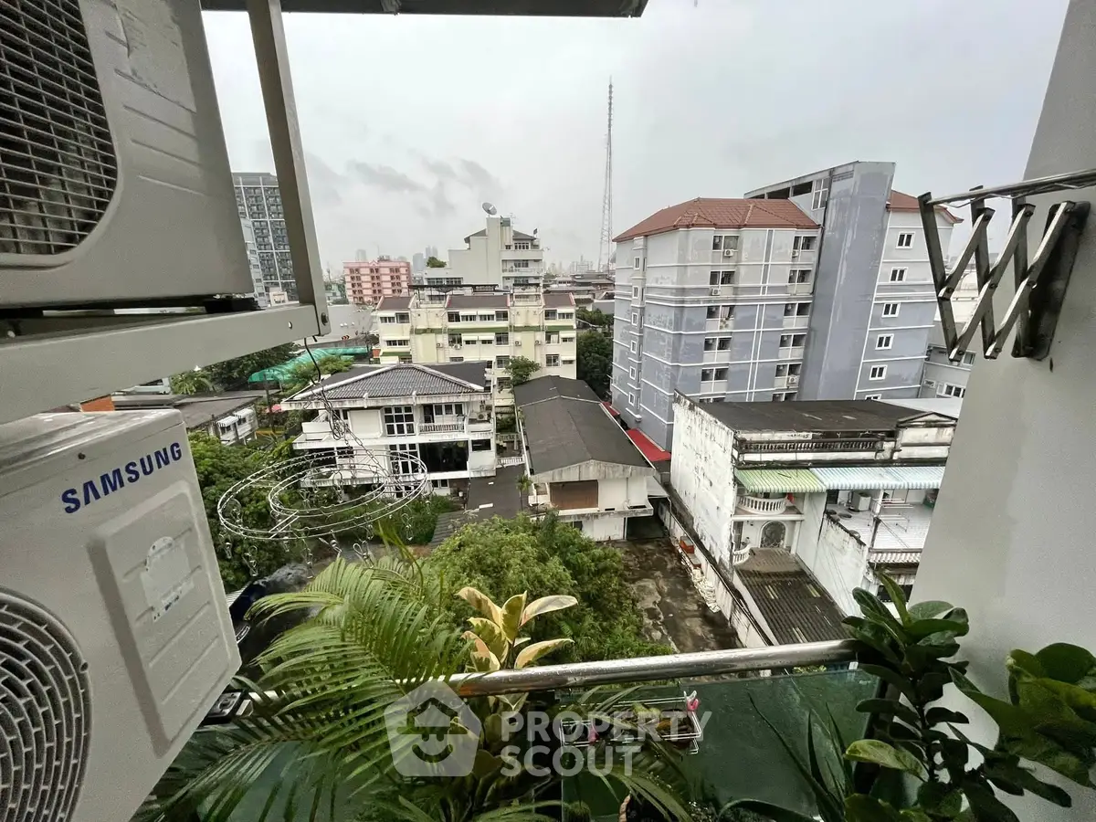 Urban view from a balcony with air conditioning units and lush greenery.