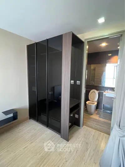 Modern bedroom with ensuite bathroom featuring sleek black wardrobe and wooden flooring.