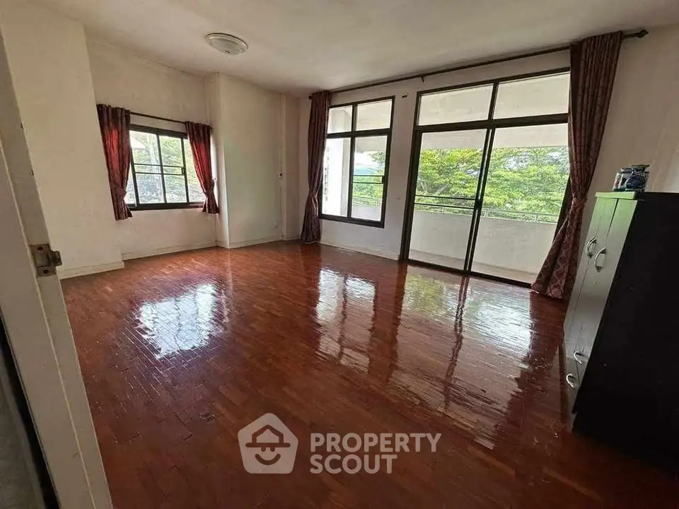 Spacious living room with polished wooden floors and large windows offering lush green views.