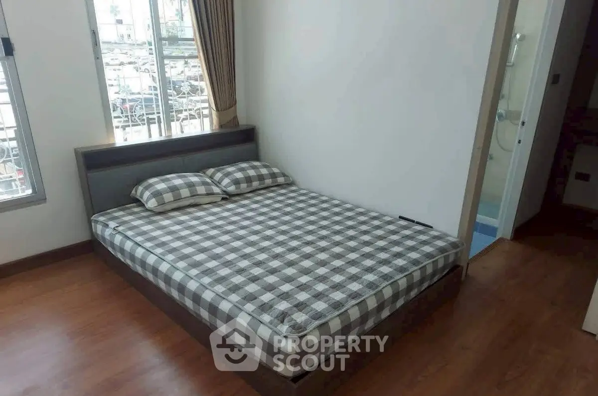 Cozy bedroom with checkered bedding and wooden flooring, featuring ample natural light from large windows.
