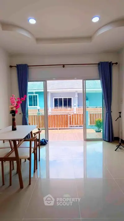 Bright living room with large glass doors opening to a spacious balcony, offering a view of modern townhouses.