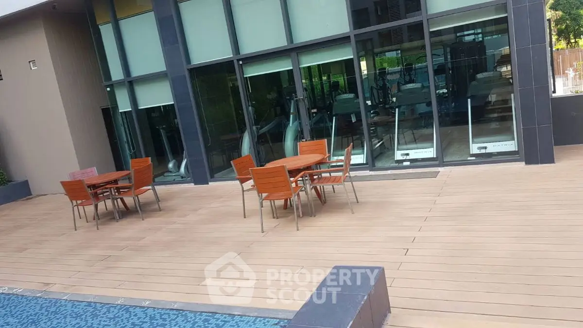 Modern poolside area with wooden deck and gym view, perfect for relaxation and fitness enthusiasts.