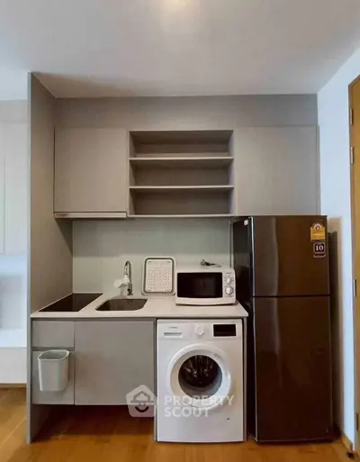 Modern compact kitchen with washing machine, fridge, and microwave in sleek apartment.