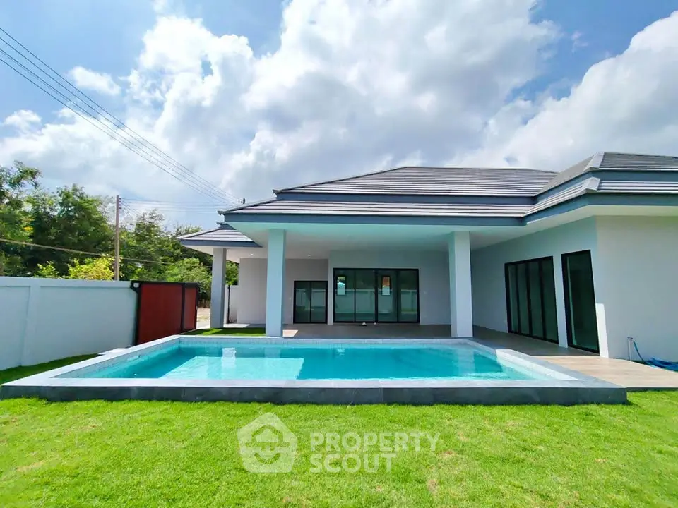 Luxurious modern home with private pool and lush green lawn under a bright blue sky.