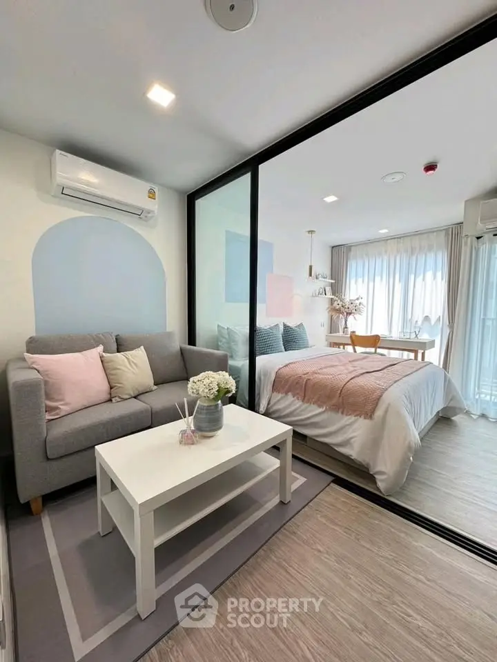 Modern studio apartment with cozy living area and stylish bedroom separated by glass partition.