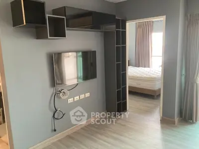 Modern apartment interior with wall-mounted TV and bedroom view, featuring sleek shelving and neutral tones.