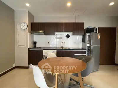 Modern kitchen with sleek cabinetry, dining table, and stainless steel appliances in a cozy apartment.